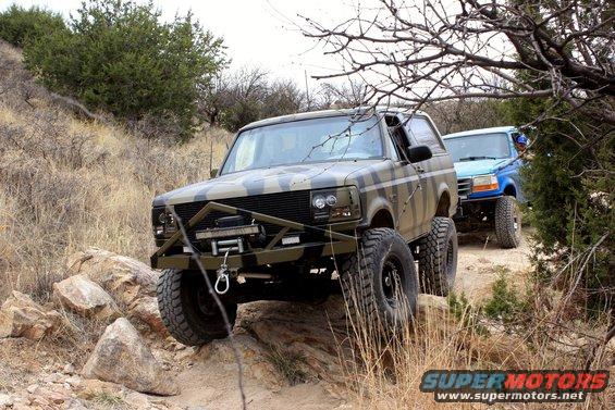 Camouflaged Ford Bronco with winch and aftermarket bumper on rocky terrain