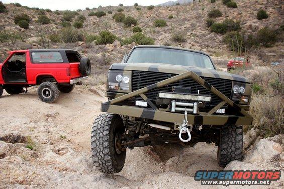 Two off-road vehicles, one camouflaged and one red, on a rocky trail