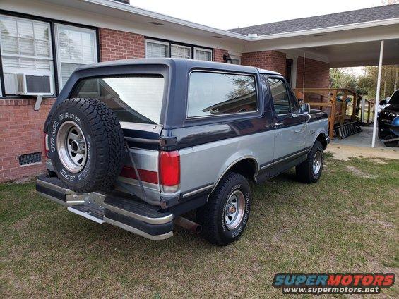 1989 Ford Bronco parked in a grassy yard next to a brick house