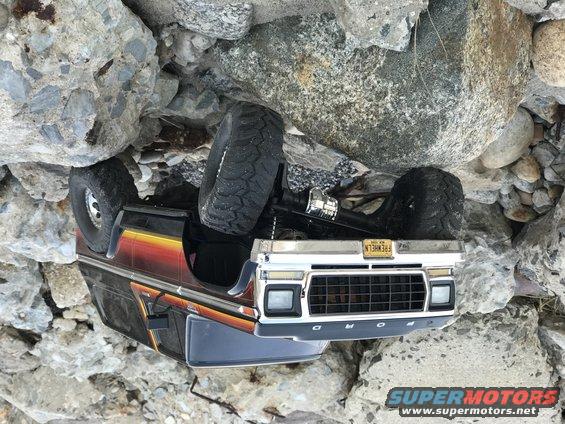 toy RC car flipped on its side among rocks. License plate reads 'FREWHEELN'
