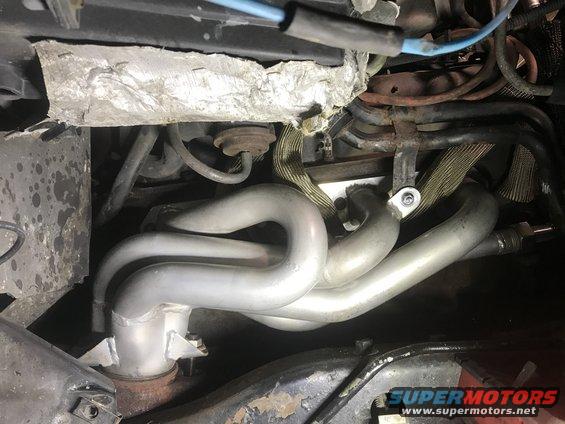 close-up of a silver exhaust manifold with pipes and engine wiring