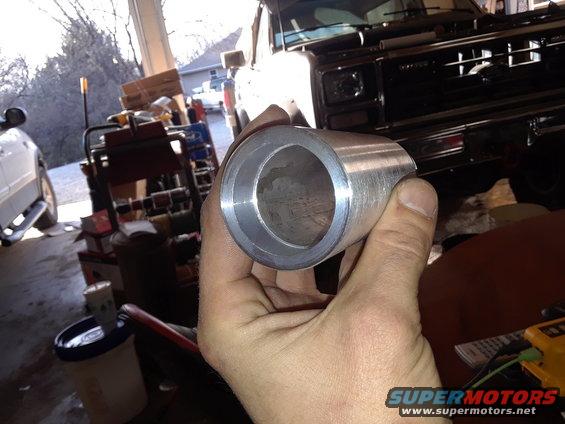 Hand holding a metal pipe fitting. A dark-colored truck is visible in the background