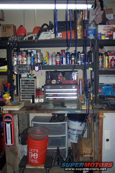 Garage workbench with shelves full of spray cans, tools, a chainsaw, and a bucket that says 'LET'S DO THIS.'