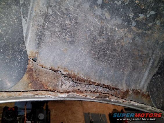 Heavily rusted wheel well interior with visible cracks and corrosion
