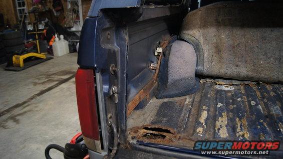 Blue pickup truck bed corner with rust and torn liner