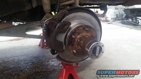 Vehicle brake assembly on red jack stand, showing rotor, caliper, and Warn hub