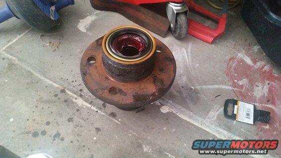 Wheel hub assembly with bearing and red grease, sitting on a concrete floor next to a tube of grease