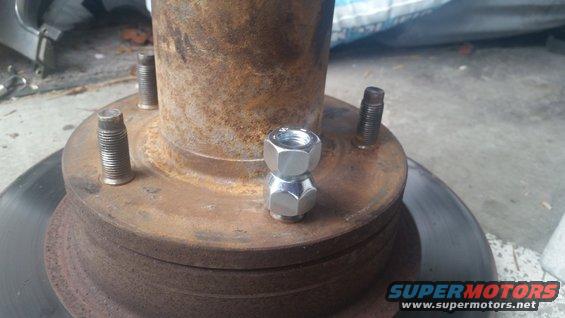 Wheel hub with two lug nuts stacked on top of each other, showing rusty metal and brake rotor