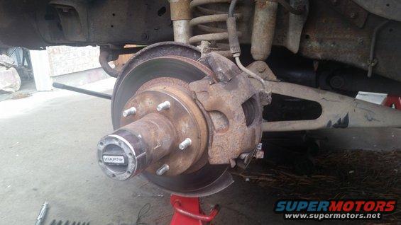 close-up of rusty vehicle brake rotor, caliper, and hub with 'WARN' text on hub