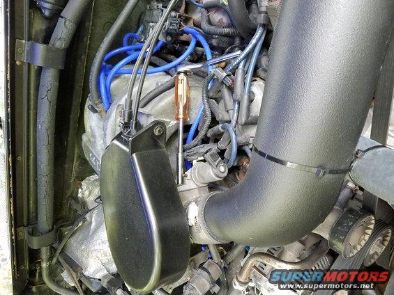 Engine bay with black intake tube, blue spark plug wires, and a screwdriver
