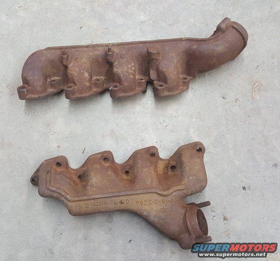 two rusty exhaust manifolds, one longer than the other, with some part numbers visible