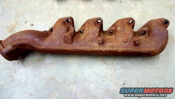 Rusty exhaust manifold with five exhaust ports and a single outlet pipe, resting on a concrete surface