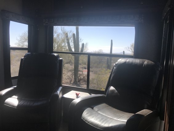 Interior of RV with two recliners, looking out at saguaro cacti and a desert landscape. An 'EXIT' sign is visible