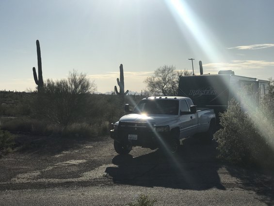 White dually pickup truck towing Pioneer travel trailer in desert landscape