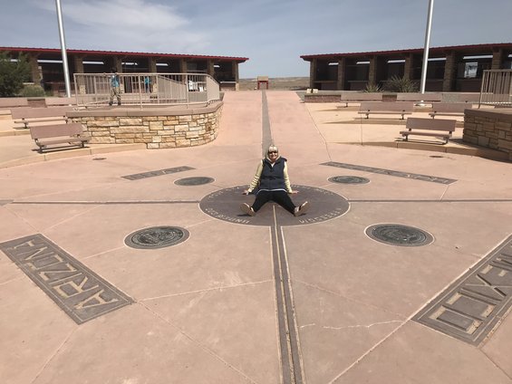 Person sitting on the ground at the Four Corners Monument, with markers for Arizona, Utah, Colorado, and New Mexico visible