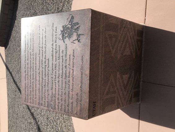 Granite monument with engraved text about the Four Corners Monument and a depiction of surveyors