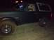 1996 Ford Bronco - A dark Ford Bronco is seen from the front-left at night, with mud on its tires.