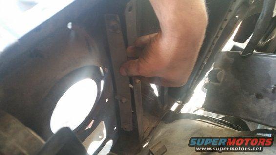 Hand reaching to adjust a metal bracket inside a vehicle's wheel well area