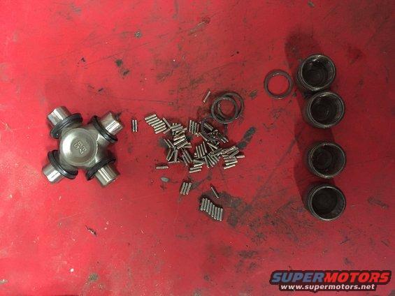 Universal joint disassembled with needle bearings, bearing cups, and seals on a red surface