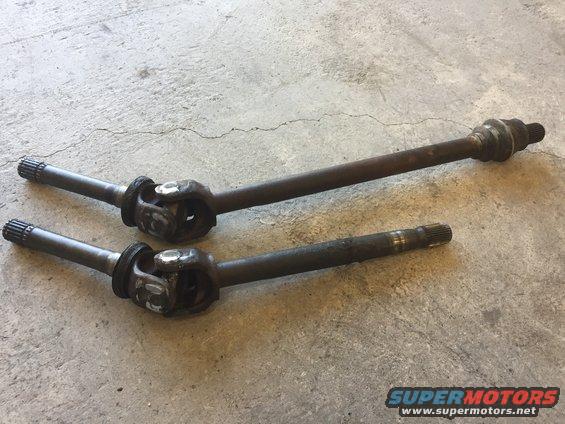 Two used drive shafts with U-joints on a concrete surface