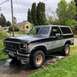 1986 Ford Bronco - This two-tone Ford Bronco is parked outside a residential home on a cloudy day.