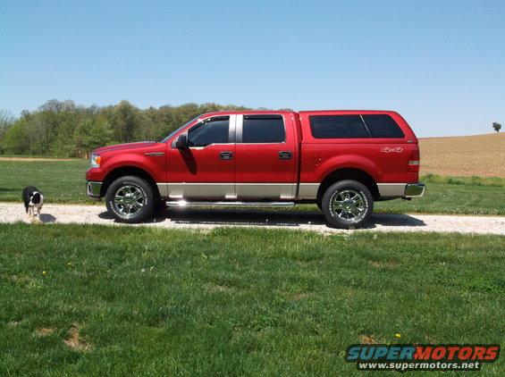 Side view of a red pickup truck with a tan lower body and a cap. A dog stands to the left