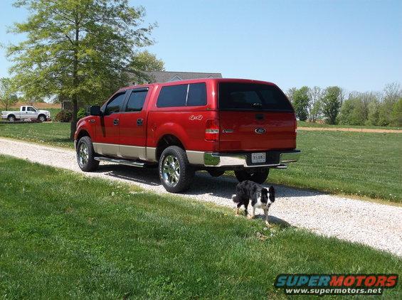 Red Ford F-150 truck with a beige lower body, camper shell, and chrome wheels parked on a gravel driveway