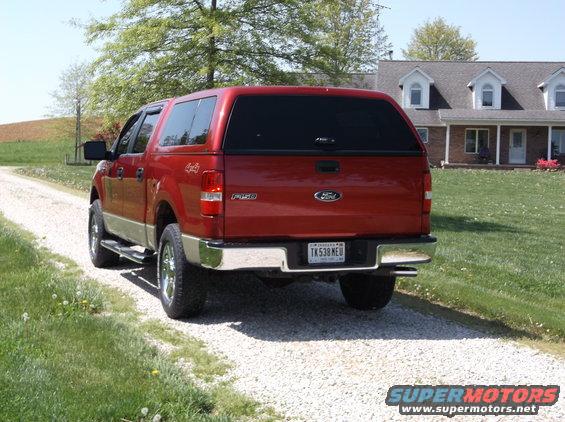 Rear view of a red Ford F-150 pickup truck with a camper shell, parked on a gravel driveway