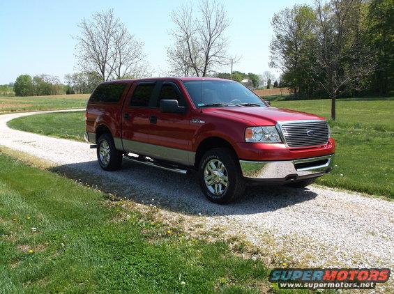 Red Ford F-150 pickup truck with a cap, parked on a gravel driveway