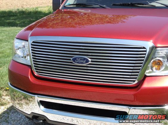 Red Ford F-150 grille and headlights, chrome bumper, some grass and dirt visible