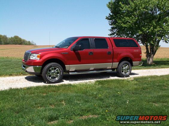 Red Ford F-150 pickup truck with a tan lower body and a matching cap, parked on a gravel driveway next to a tree