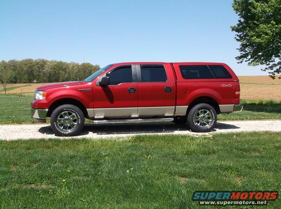 Red pickup truck with a tan lower body and a cap, parked on a gravel driveway