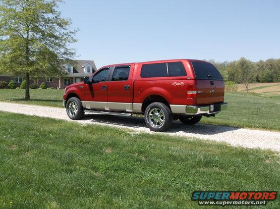 Red Ford F-150 pickup truck with a tan lower body and a black camper shell, parked on a gravel driveway