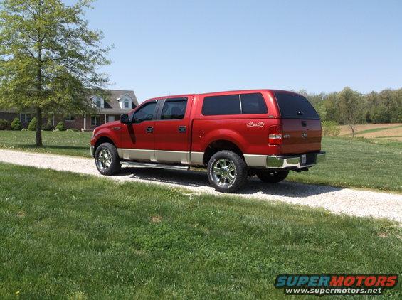 Red pickup truck with a tan lower body and a cap, parked on a gravel driveway
