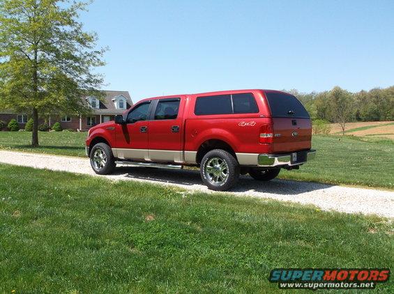 Red and tan Ford F-150 truck with a camper shell parked on a gravel driveway