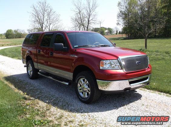Red Ford F-150 pickup truck with a silver two-tone lower body and a camper shell, parked on a gravel driveway