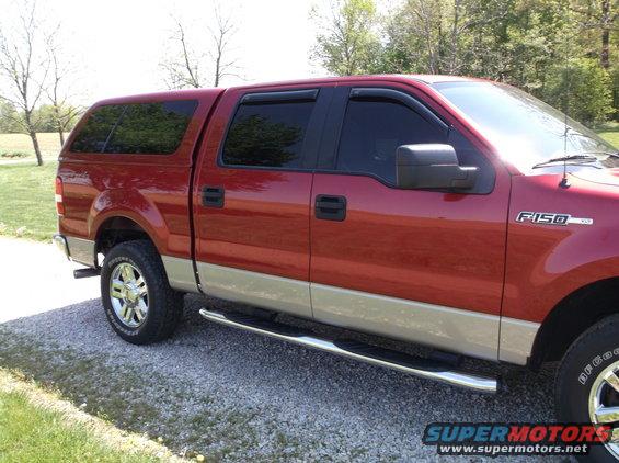 Red Ford F-150 pickup truck with a tan lower body and a cap, parked on a gravel driveway