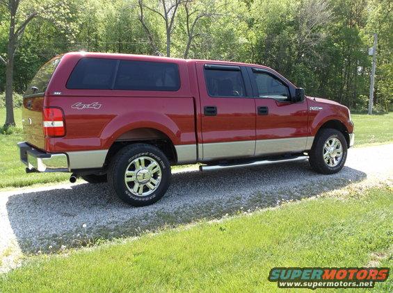Red Ford F-150 pickup truck with tan lower body, camper shell, and chrome wheels, parked on a gravel driveway