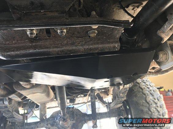 Underbody view of a vehicle showing a skid plate installed over the transfer case, with suspension components visible