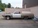 1971 Ford Ranchero - A tan and white 1971 Ford Ranchero is parked outside a building, its hood covered with tarps and a mattress in the bed.