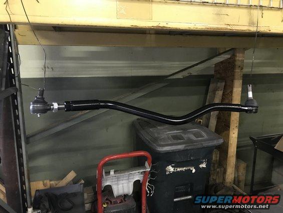 Black tie rod with ball joints on each end, hanging in a workshop