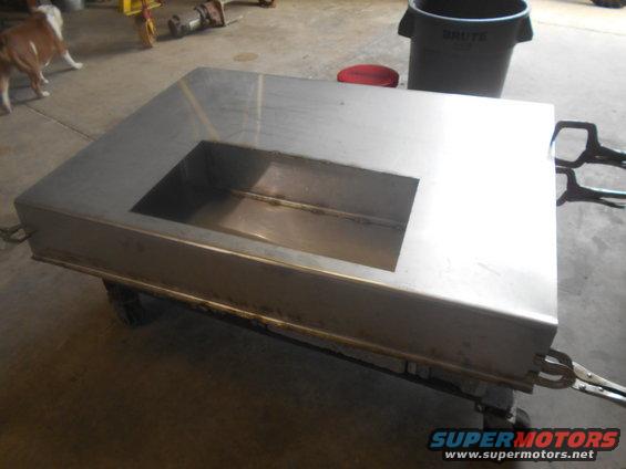 Metal fabrication on wheels with a rectangular cutout, viewed from a 3/4 front angle. A dog is in the background