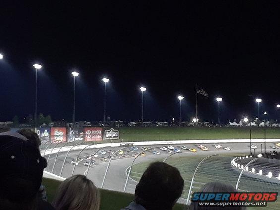 Race cars on a track at night with stadium lights