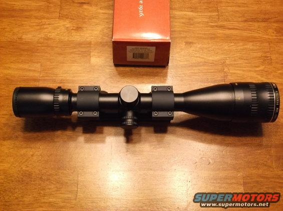 Rifle scope with mounting rings and an orange box on a wooden surface