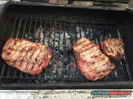 Three steaks grilling over hot coals