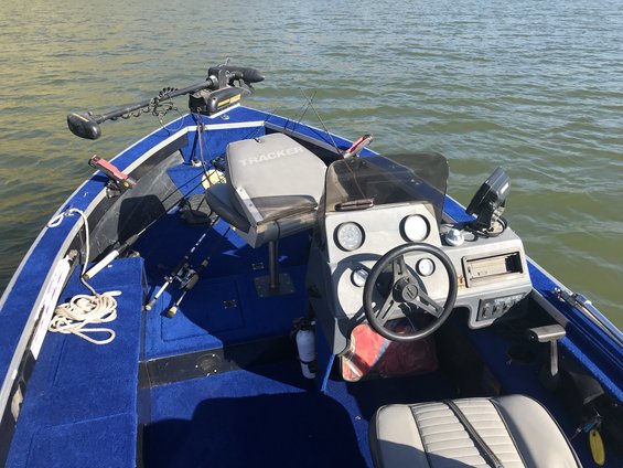 Boat interior with blue carpet, captain's seat, steering wheel, and trolling motor