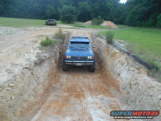 Blue SUV driving down a dirt ditch. Another vehicle is visible in the background