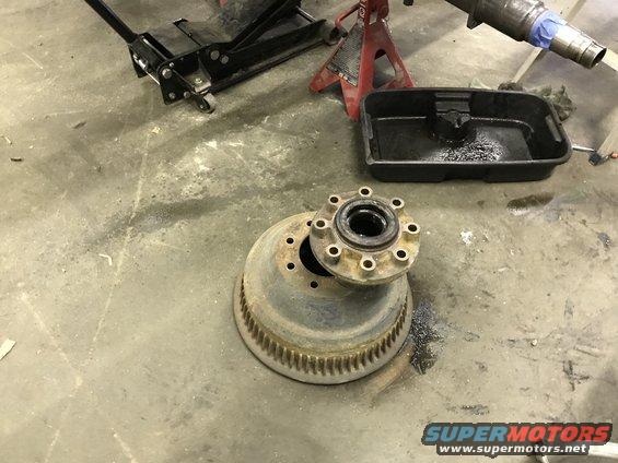 truck brake drum and hub assembly on concrete floor with jack and drain pan