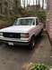 1990 Ford Bronco - A white Ford Bronco is parked in a driveway next to a pink house, with a wooded hill in the background.