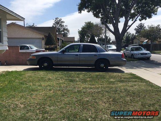 Gray sedan parked on a grassy lawn, side view. Black wheels, tinted windows